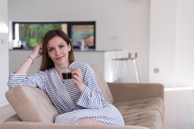 Bella giovane donna in accappatoio che si gode il caffè del mattino nella sua lussuosa villa domestica