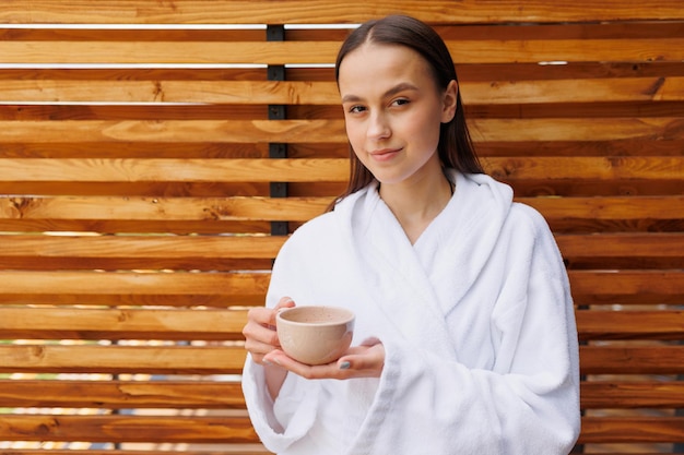 Bella giovane donna in accappatoio e una tazza di tè in mano beve il tè del mattino