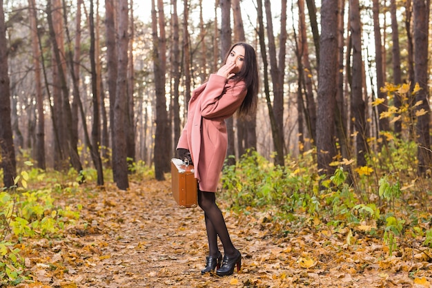 Bella giovane donna in autunno parco in posa con la valigia