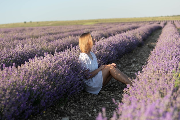 Bella giovane donna in camicia bianca seduta in un campo di lavanda