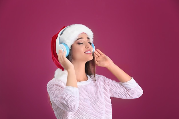 Bella giovane donna in cappello di Babbo Natale che ascolta la musica di Natale