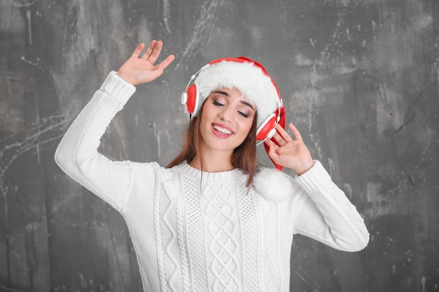 Bella giovane donna in cappello di Babbo Natale che ascolta musica di Natale su sfondo grunge grunge