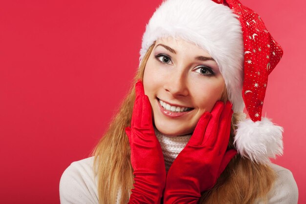 Bella giovane donna in cappello di Babbo Natale e guanti sorridente Racconto di Natale Sfondo rosso Postcard Spazio per il testo