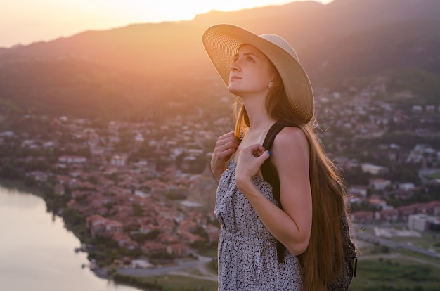 Bella giovane donna in cappello sul panorama della città del tramonto. vista laterale