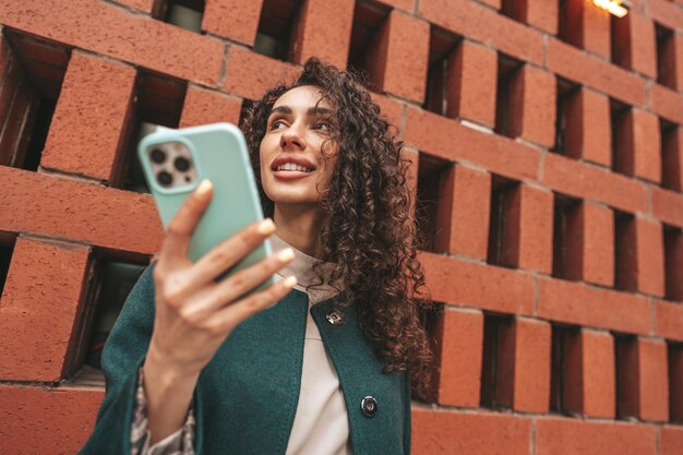 Bella giovane donna in cappotto verde usando il suo cellulare in città