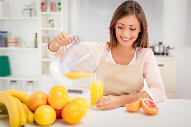 Bella giovane donna in cucina che spreme il succo d'arancia con uno spremiagrumi elettrico. Sta versando il succo in un bicchiere.