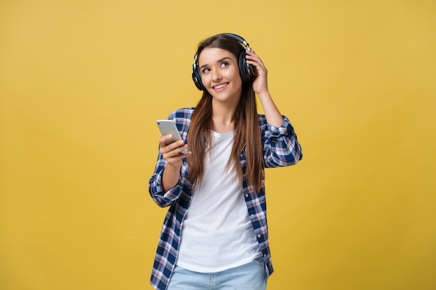 Bella giovane donna in cuffie ascoltando musica e cantando su sfondo giallo