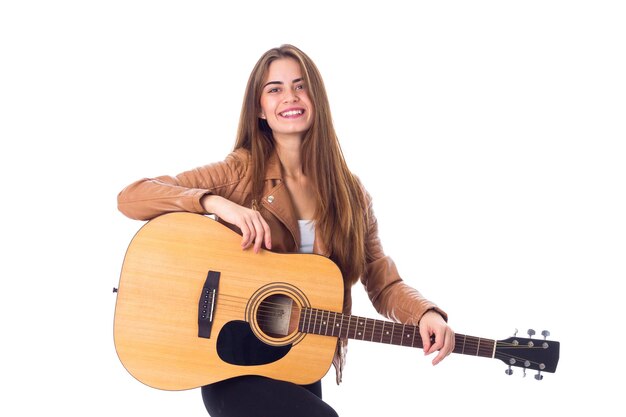 Bella giovane donna in giacca marrone e pantaloni neri che suona la chitarra in studio