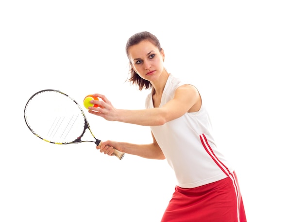Bella giovane donna in gonna rossa con coda di cavallo castagna che tiene racchetta da tennis e palla gialla