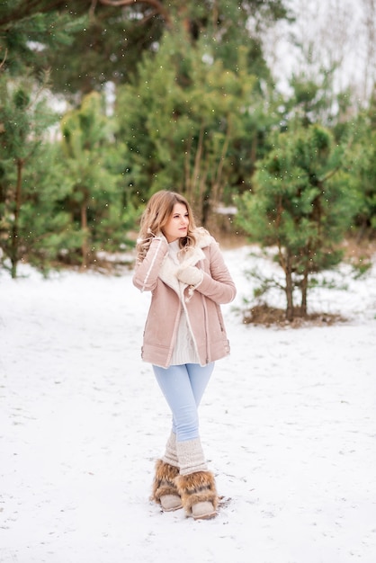 Bella giovane donna in jeans e giacca rosa nella foresta invernale