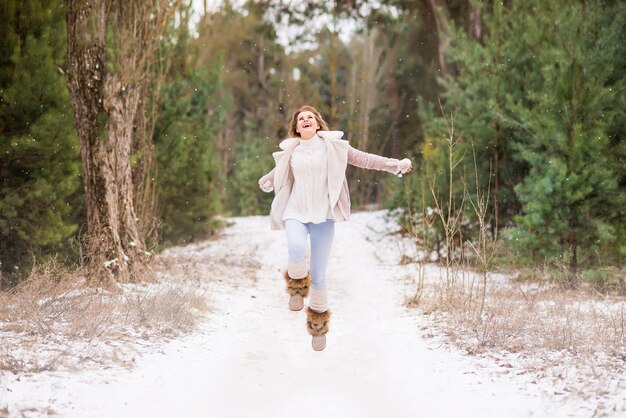 Bella giovane donna in jeans e giacca rosa nella foresta invernale