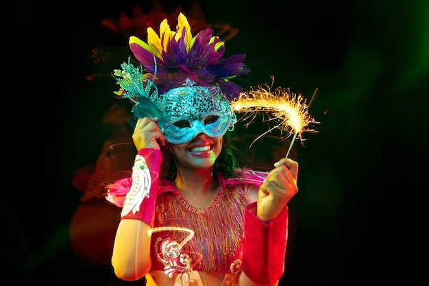 Bella giovane donna in maschera di carnevale e costume in maschera con luci colorate