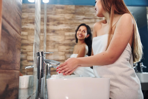 Bella giovane donna in piedi in bagno vicino allo specchio e lavarsi le mani. Amici dietro.