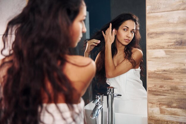 Bella giovane donna in piedi in bagno vicino allo specchio.