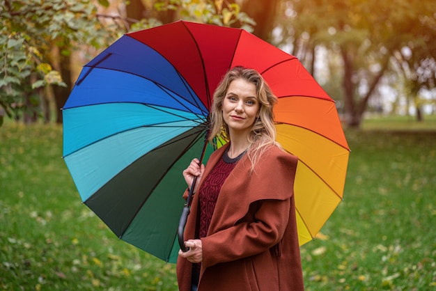 Bella giovane donna in piedi nel parco sotto un ombrello color arcobaleno. Una bella ragazza cammina