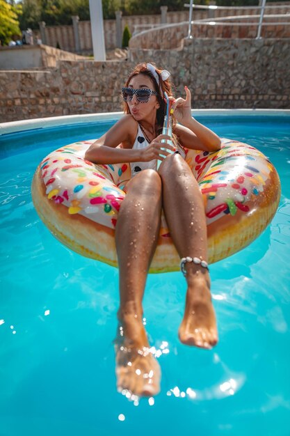 Bella giovane donna in piscina nuota sulla ciambella gonfiabile e si diverte in acqua in vacanza.