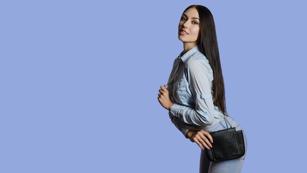 Bella giovane donna in posa in studioin jeans con borsa