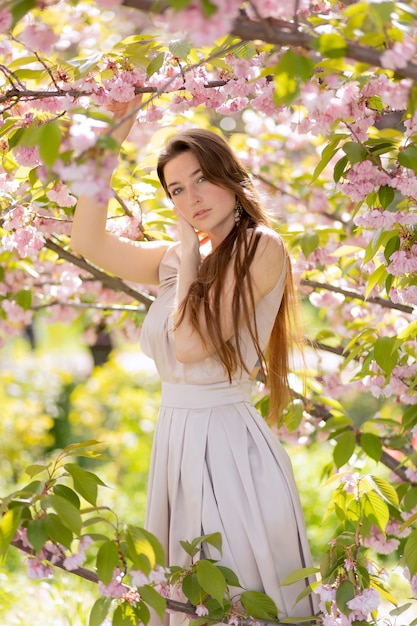 Bella giovane donna in posa in un giardino fiorito di sakura.