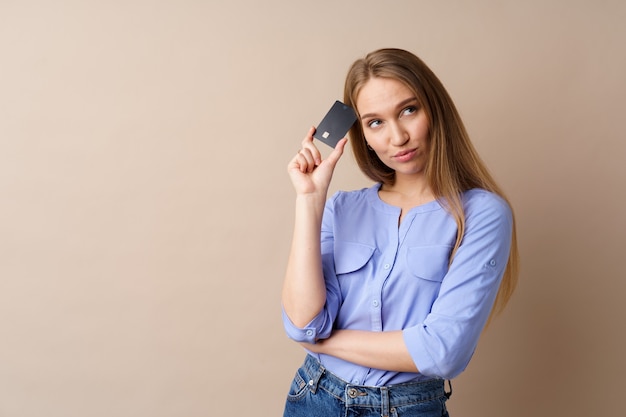 Bella giovane donna in possesso di carta di credito nera su sfondo beige