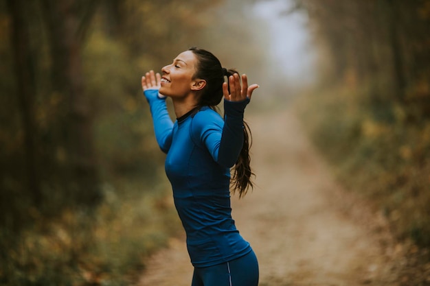 Bella giovane donna in tuta blu che allarga le braccia e fa un respiro profondo in una foresta