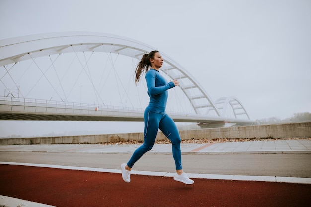 Bella giovane donna in tuta blu che corre lungo il fiume al mattino d'autunno