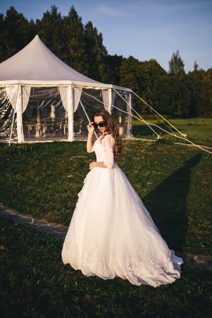 Bella giovane donna in un abito da sposa bianco e stivali neri al tramonto.