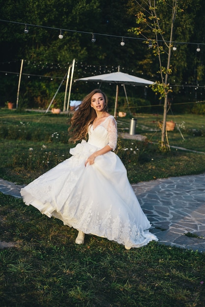 Bella giovane donna in un abito da sposa bianco e stivali neri al tramonto.