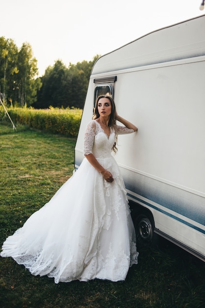 Bella giovane donna in un abito da sposa bianco e stivali neri al tramonto.