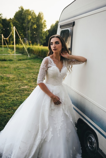 Bella giovane donna in un abito da sposa bianco e stivali neri al tramonto.