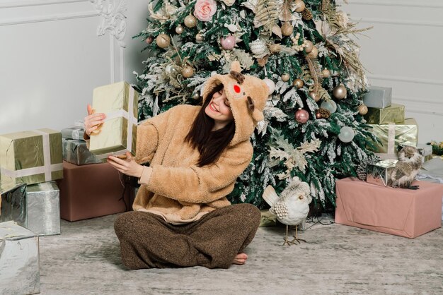 Bella giovane donna in un abito elegante in piedi accanto all'albero di Natale e regali.