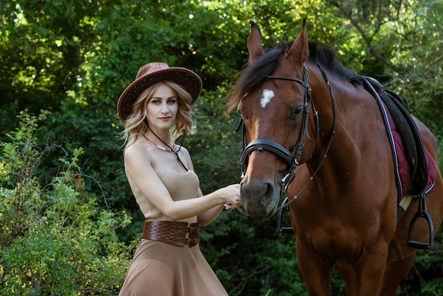 Bella giovane donna in un cappello da cowboy vicino a un cavallo sulla natura nel parco