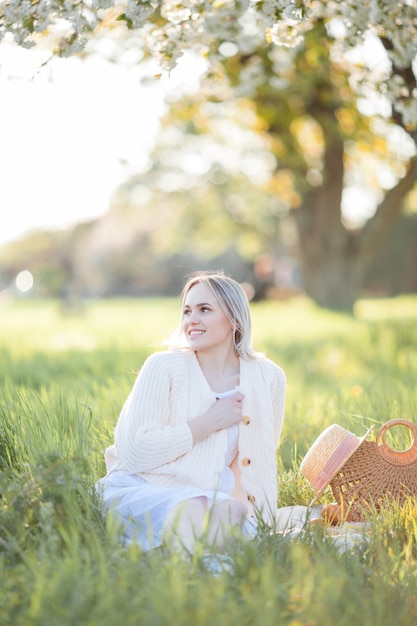 Bella giovane donna in un cappello di vimini sta riposando su un picnic in un giardino fiorito