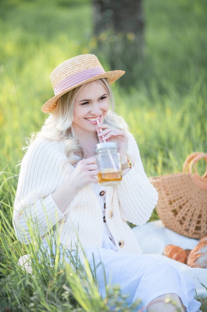 Bella giovane donna in un cappello di vimini sta riposando su un picnic in un giardino fiorito