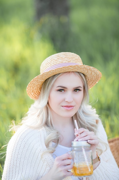 Bella giovane donna in un cappello di vimini sta riposando su un picnic in un giardino fiorito