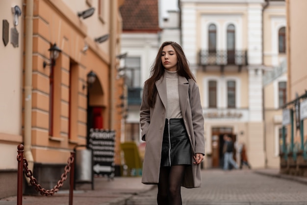 Bella giovane donna in un cappotto elegante con un'elegante borsetta nera si trova in una strada della città