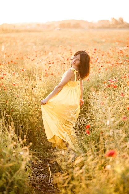 Bella giovane donna in un vestito giallo che cammina in un campo di papaveri in una giornata estiva. Ragazza che gode dei fiori in campagna. Messa a fuoco selettiva