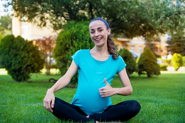 Bella giovane donna incinta calma è seduta nella posizione del loto e medita mentre pratica yoga nel parco