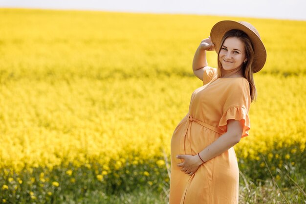 Bella giovane donna incinta in un campo di colza giallo.