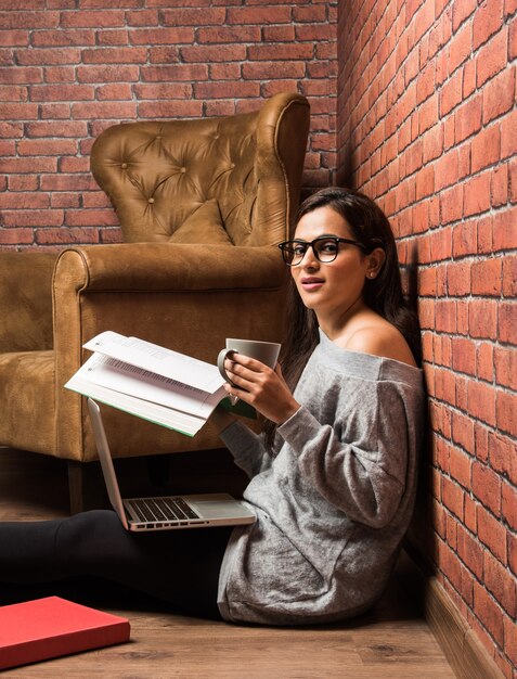 Bella giovane donna indiana o asiatica che studia con un libro e un laptop sul pavimento