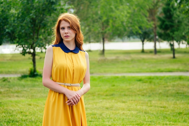 Bella giovane donna irlandese della testarossa dello zenzero in un vestito giallo alla moda nel parco di estate. concetto di freschezza e femminilità