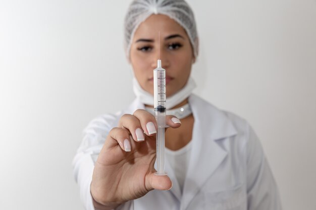 Bella giovane donna medico in camice medico e una maschera protettiva e siringa.