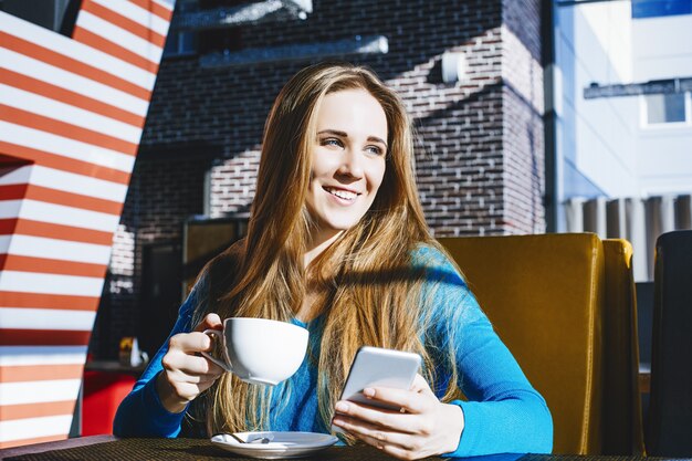 Bella giovane donna moda di successo e bella con un telefono cellulare e una tazza di caffè in un bar