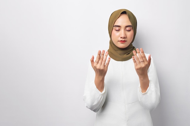 Bella giovane donna musulmana asiatica araba che indossa l'hijab che prega a braccia aperte chiedendo preghiera per qualcosa di isolato su sfondo bianco Concetto di stile di vita religioso della gente