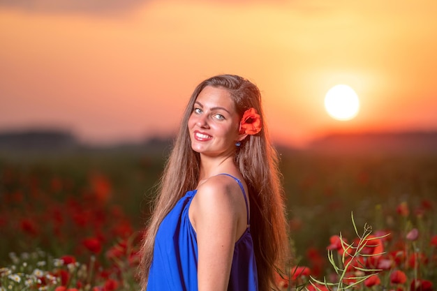 Bella giovane donna nel campo di papaveri con il paesaggio al tramonto nella calda luce del tramonto sullo sfondo