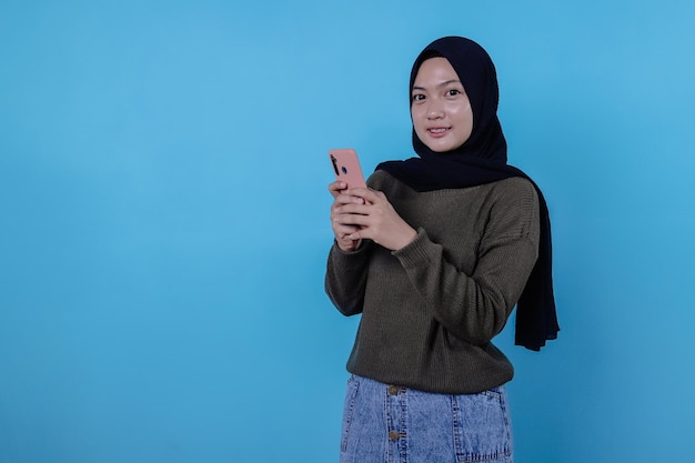Bella giovane donna positiva dall'aspetto amichevole che indossa l'hijab con un bel sorriso sincero che si sente grata e grata tenendo il telefono cellulare