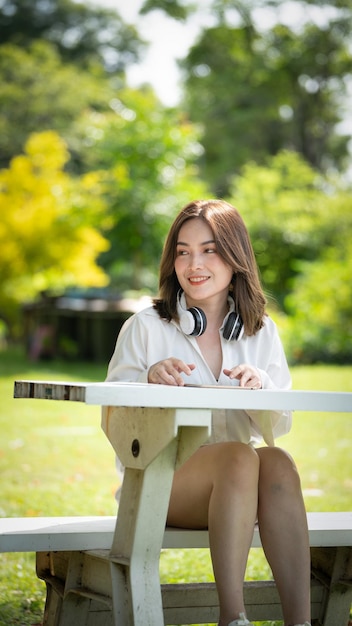 Bella giovane donna ragazza in camicia beige in posa sullo sfondo del parco della città verde Sorriso ragazza che ascolta musica con le cuffie sensazione toccante felicità concetto di stile di vita persone Mock up spazio di copia