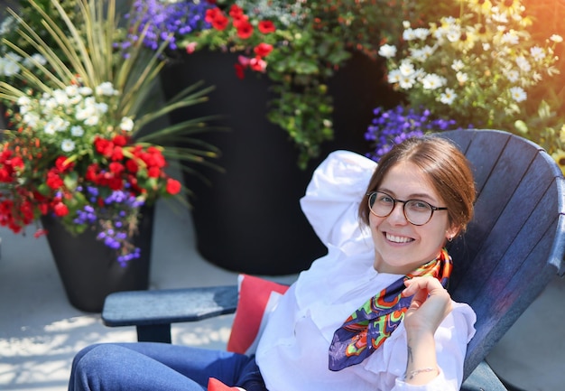 Bella giovane donna riposa in un caffè all'aperto guardando i fiori della fotocamera su uno sfondo