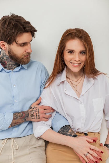 Bella giovane donna rossa felice e brutale uomo alla moda hipster con barba e tatuaggio in abiti alla moda su sfondo bianco