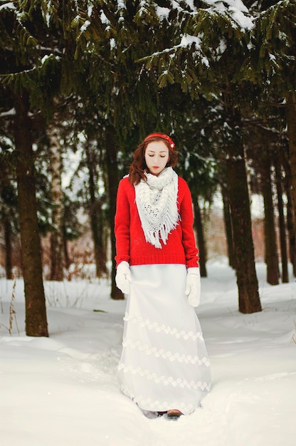 Bella giovane donna rossa in maglione verde e abito da sposa bianco che cammina nel gelido inverno park