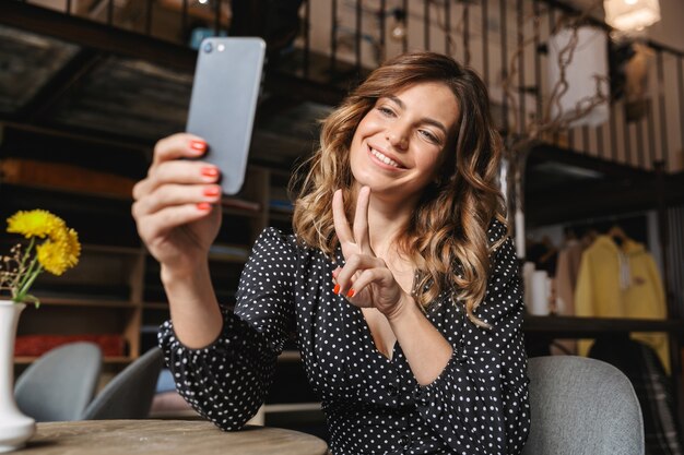 Bella giovane donna seduta al caffè al chiuso, prendendo un selfie